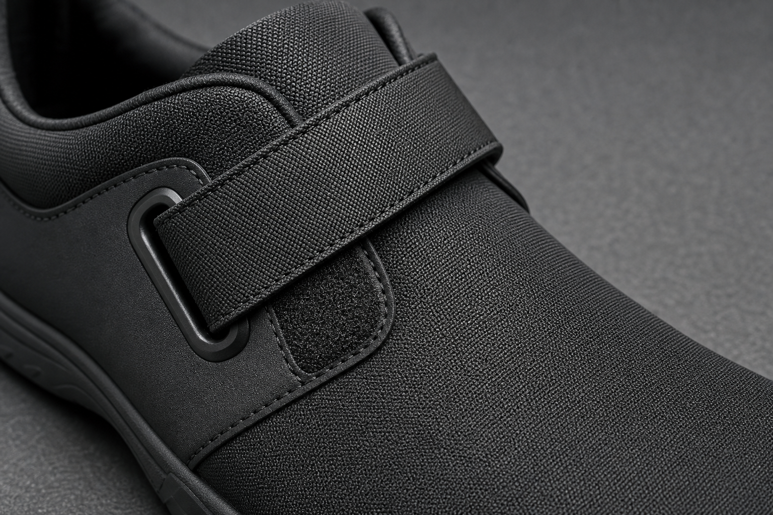 Macro view of a wide adjustable strap closure with low-profile hook-and-loop fastening on a wipeable synthetic upper